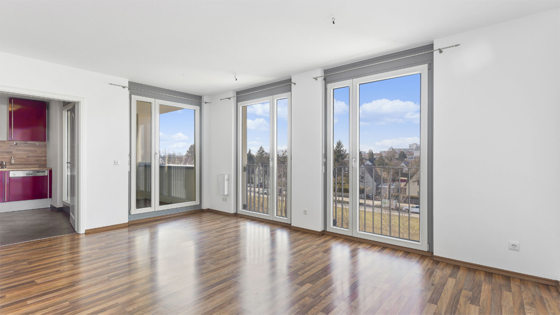 Unmöblierter Wohnraum mit Balkontüren und Durchblick zur roten Küchenzeile in einer Wohnung in München-Milbertshofen