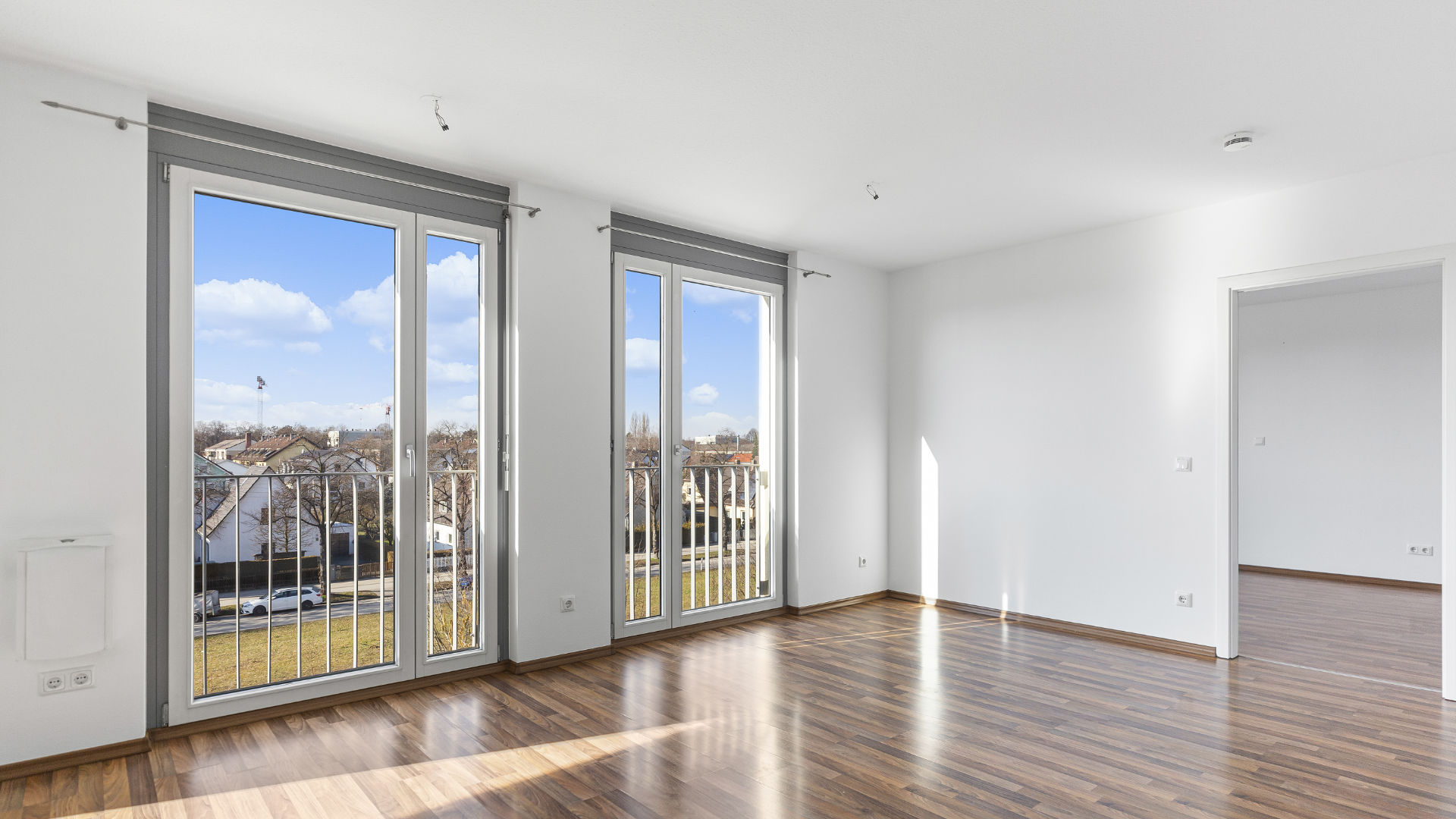 Unmöblierter Wohnraum mit zwei Balkontüren, Glasgeländer und Parkettboden in einer Wohnung in München-Milbertshofen