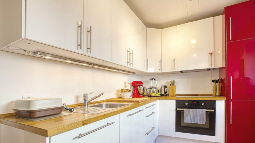 Kitchen in the apartment in Munich-Obersendling with white kitchen island, wooden worktop and red refrigerator