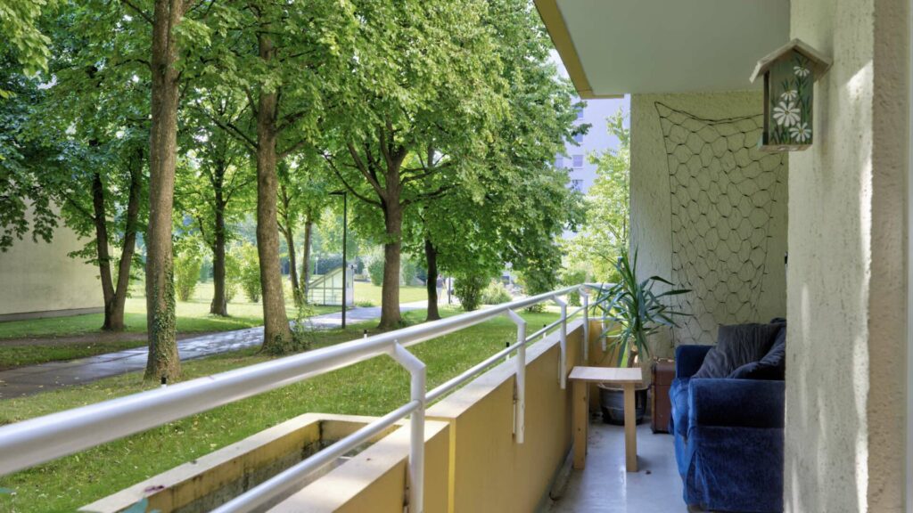 Balcony with dark blue chair and small plant, view over railings to trees and road in Perlach