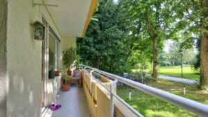 Balcony with wooden railings and a view over a green area with trees onto a street in Perlach