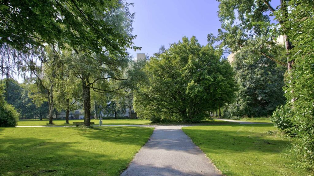 Paved path through a green park with trees in the residential area in Munich-Perlach