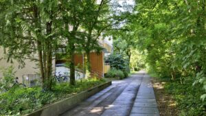 Paved path between trees leads to a building with orange-colored window shutters in Munich-Perlach
