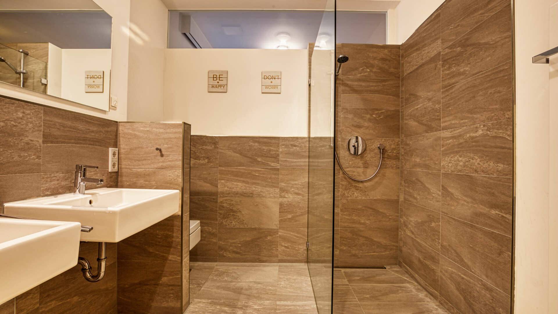 Modern shower room with natural stone tiles and a glass shower wall in the apartment in Munich-Schwabing – Rogers Immobilien