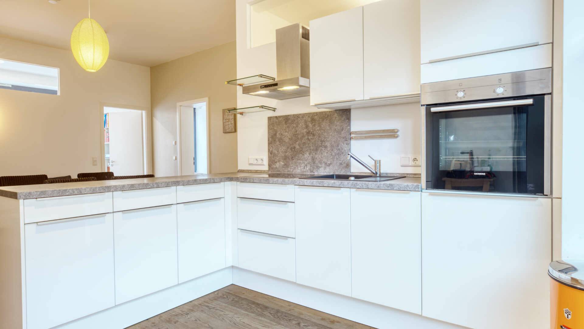 L-shaped fitted kitchen with granite worktop and light wooden floor in the apartment in Schwabing – Rogers Immobilien