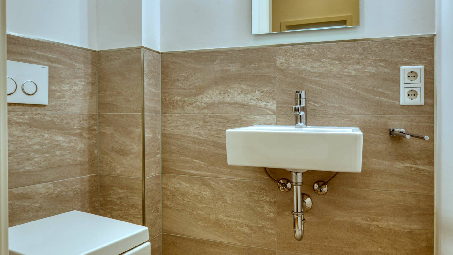 Guest toilet with washbasin and natural stone tiles in the owner-occupied apartment in Munich-Schwabing – Rogers Immobilien