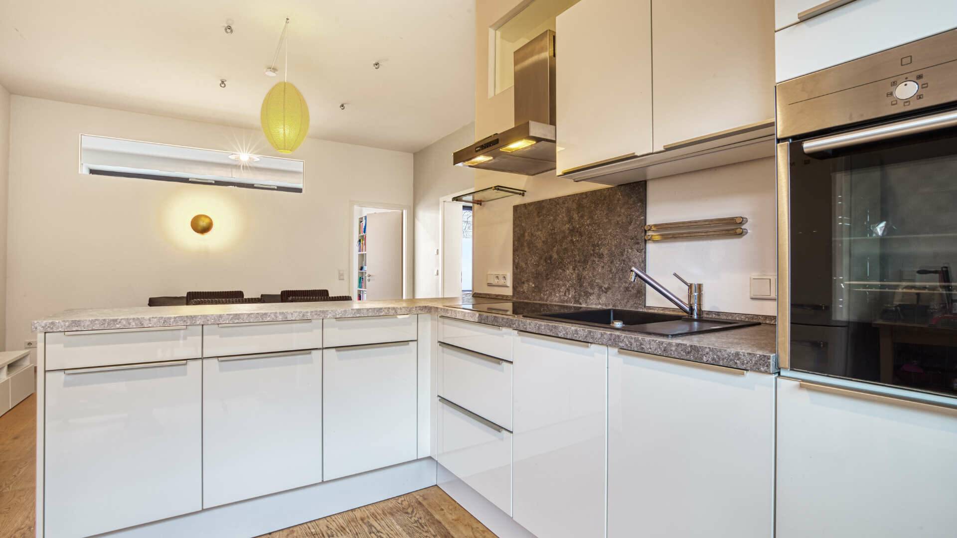 White built-in kitchen in L-shape with granite worktop and oven in the apartment in Schwabing – Rogers Immobilien