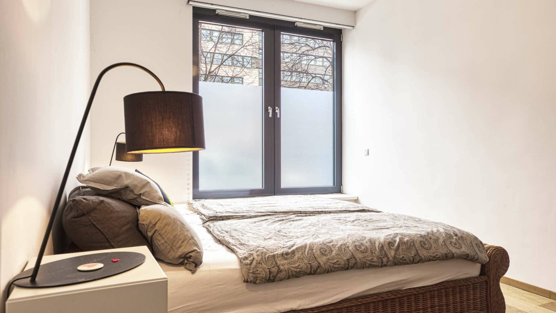 Bedroom detail with bed, patterned blanket and floor lamp with dark shade in apartment in Schwabing – Rogers Immobilien