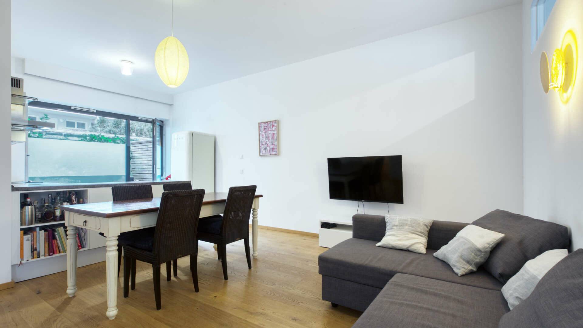 Living/dining area with large window front, white table and grey sofa in the apartment in Schwabing – Rogers Immobilien