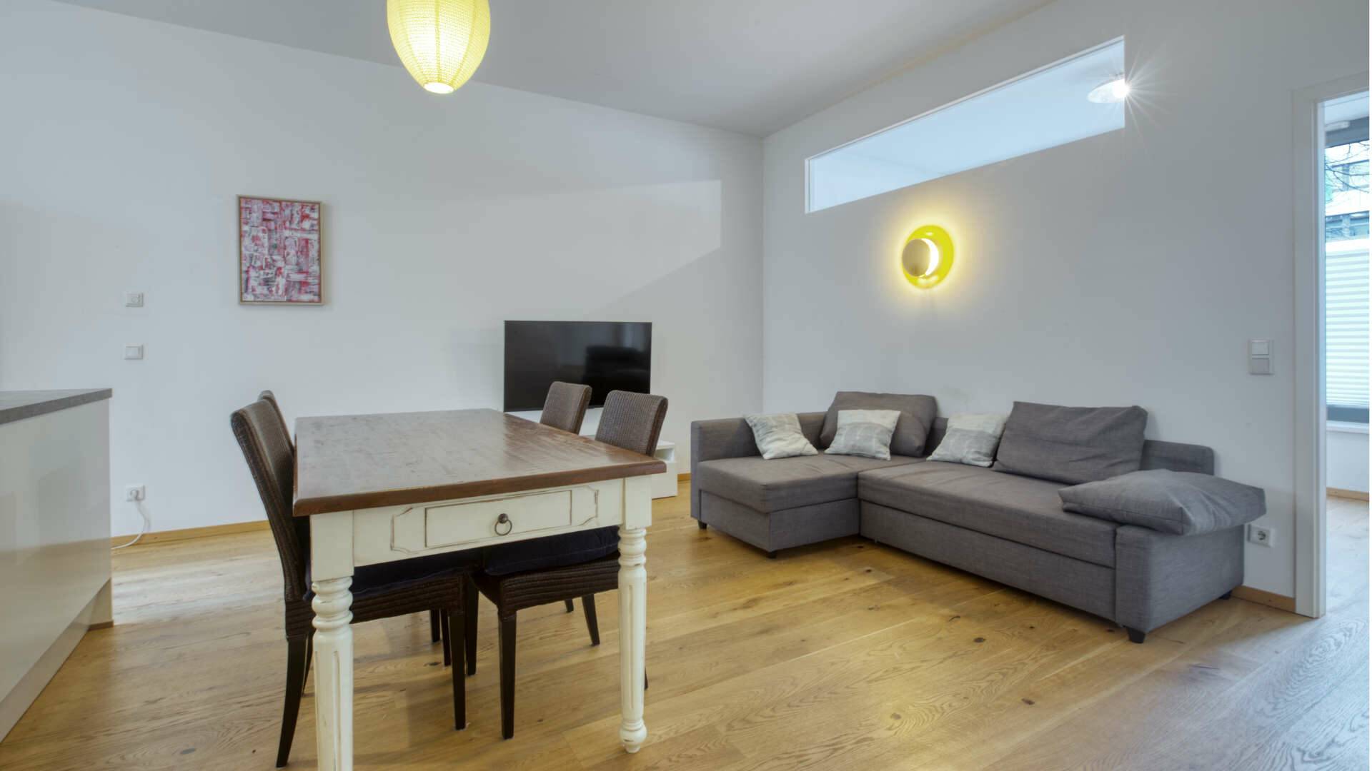 Overall view of the living and dining area with a bright table and grey couch in the apartment in Schwabing – Rogers Immobilien