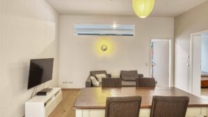 Living room with TV, armchairs and rattan chairs at the dining table in the apartment in Schwabing – Rogers Immobilien