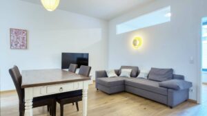 Living room with gray corner sofa, dining table and TV in the apartment in Schwabing – Rogers Immobilien
