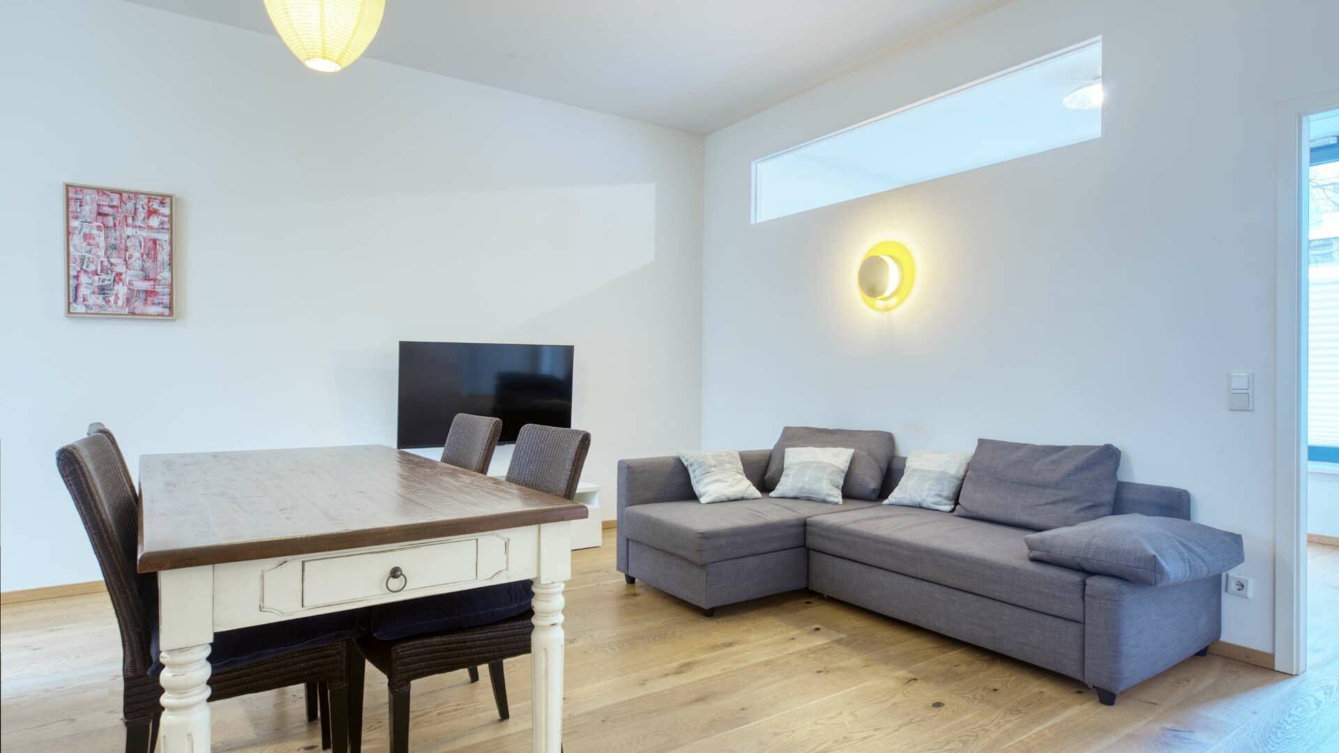 Living room with gray corner sofa, dining table and TV in the apartment in Schwabing – Rogers Immobilien