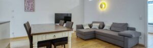 Panorama view of living room and dining area with gray couch and dining table in the apartment in Schwabing – Rogers Immobilien