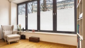 Empty room with armchair, pleated curtains and bookshelf in the apartment in Schwabing – Rogers Immobilien