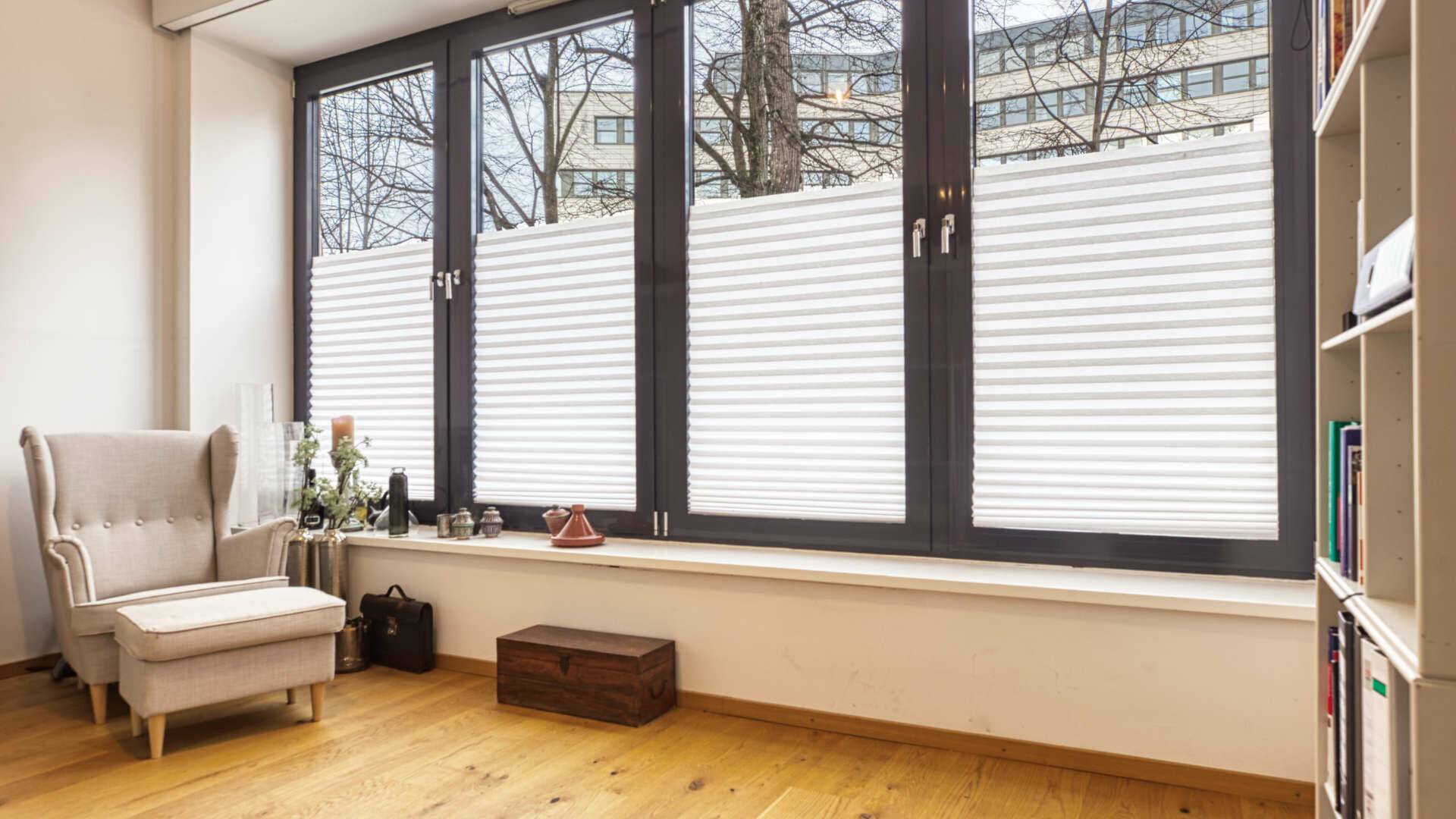 Empty room with armchair, pleated curtains and bookshelf in the apartment in Schwabing – Rogers Immobilien