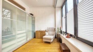 Room with sliding door wardrobe and armchair by the window in the Munich-Schwabing apartment – Rogers Immobilien