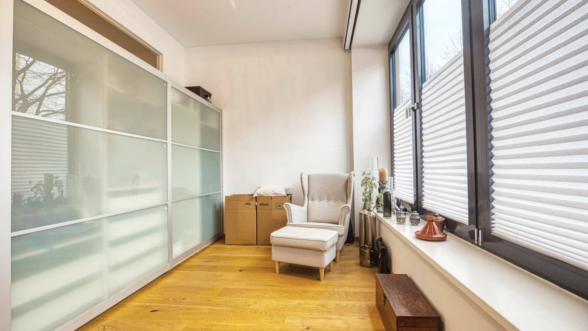 Room with sliding door wardrobe and armchair by the window in the Munich-Schwabing apartment – Rogers Immobilien