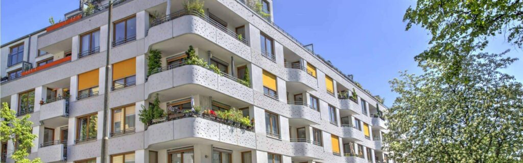 Straßenansicht des Wohngebäudes in Sendling mit weißer Fassade, gelben Sonnenschutz-Markisen und Bäumen