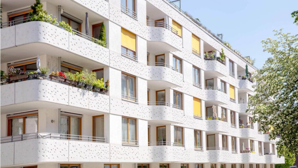 Außenansicht des Wohngebäudes in Sendling mit weißer Fassade, gelben Markisen und begrünten Balkonen