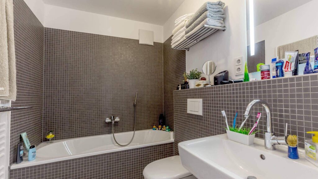 Badezimmer der Wohnung in Sendling mit dunklen Mosaikfliesen, Badewanne, WC und Waschbecken