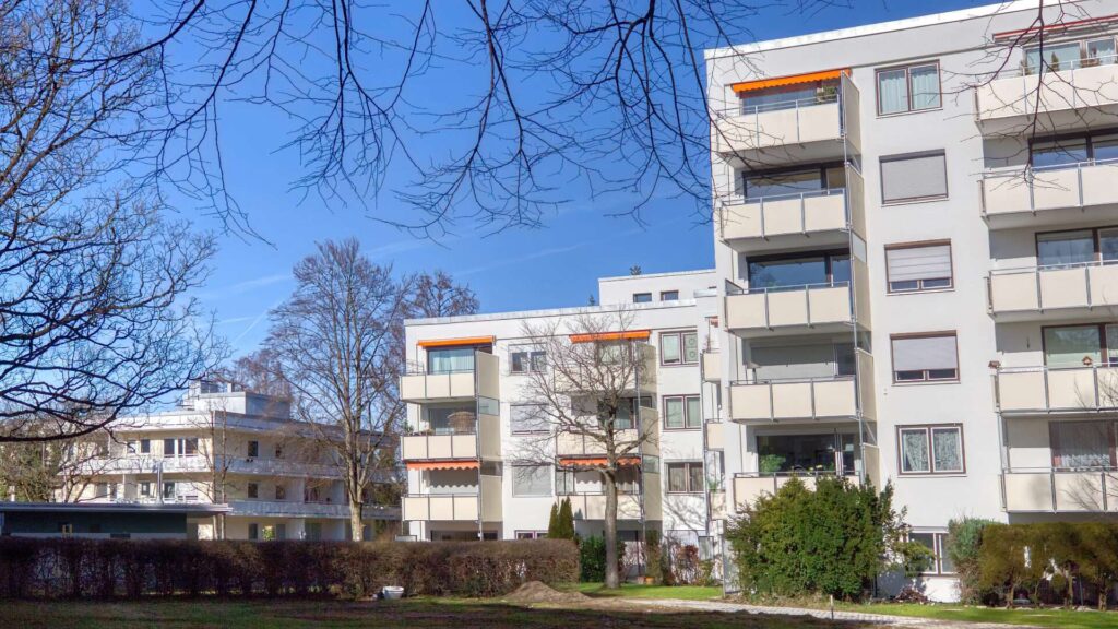 Wohnhaus mit Balkonen und gepflegter Grünanlage unter blauem Himmel in Solln