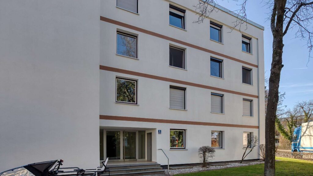 Weißes Mehrfamilienhaus mit Eingangstür und Terrassenzugang im Erdgeschoss, Solln