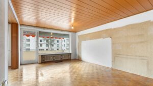 Leeres Wohnzimmer mit Holzvertäfelung an der Decke und Parkettboden, unrenoviert, in Solln