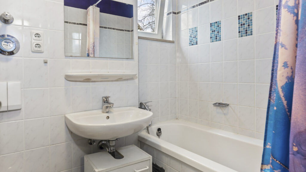 Bathroom of the apartment in Munich-Untermenzing with washbasin, toilet, and bathtub with a patterned shower curtain