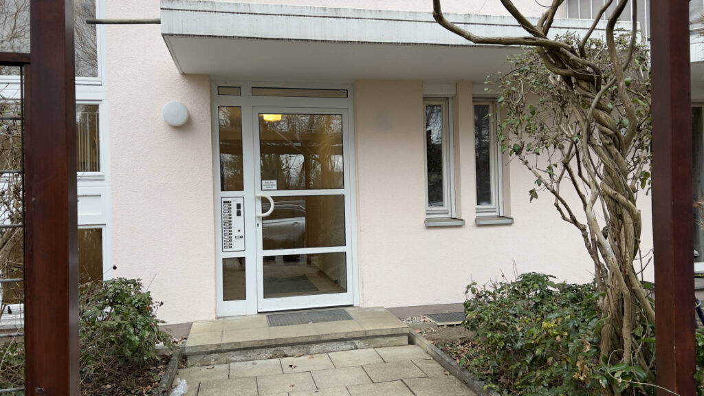 Entrance area of the residential building in Munich-Untermenzing with a double glass door and salmon-colored facade