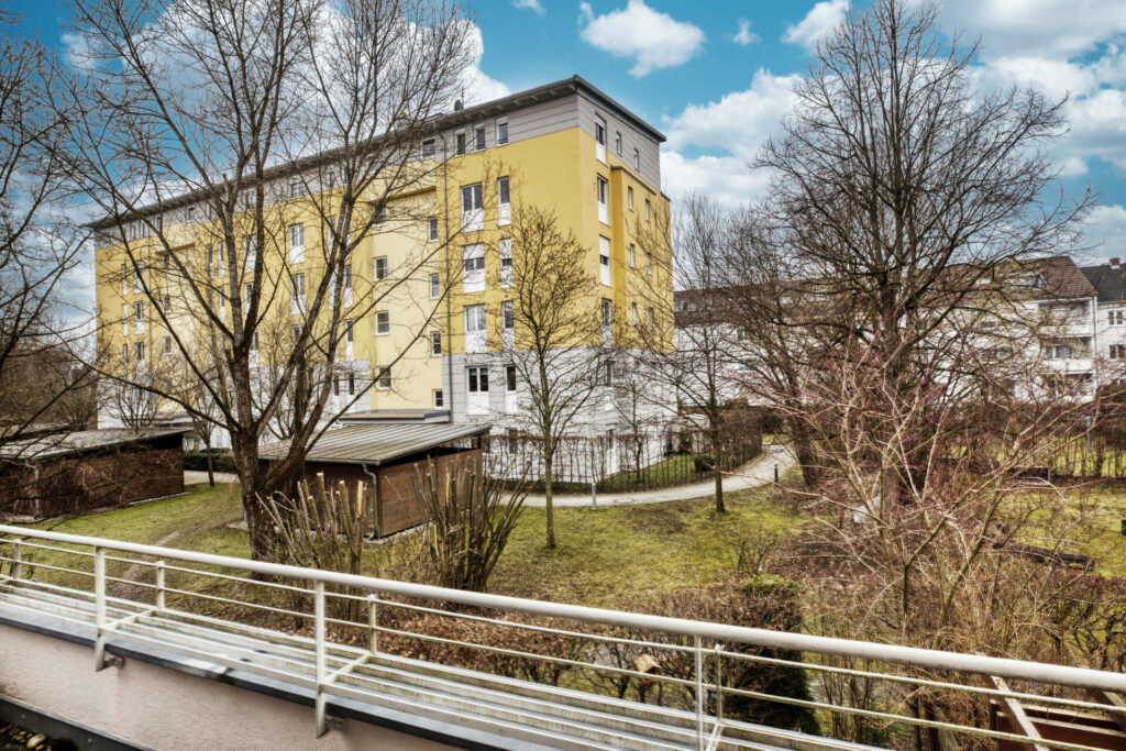 Pedestrian bridge overlooking a yellow residential building surrounded by greenery in the Untermenzing district of Munich