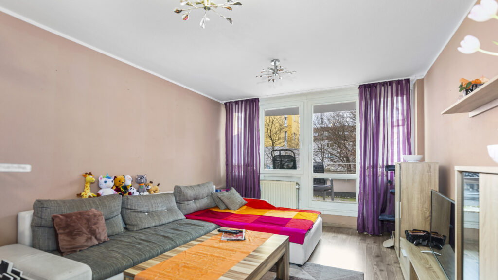 Living room of the apartment in Munich-Untermenzing with a gray sectional sofa, salmon-colored walls, and purple curtains