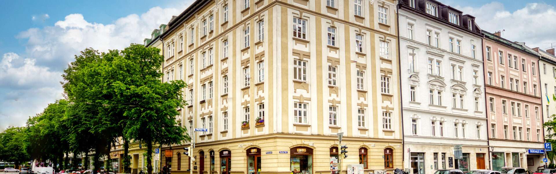 Historisches Eckhaus mit gelber und rosa Fassade an einer Münchner Straßenkreuzung – geerbte Immobilie verkaufen mit Rogers Immobilien