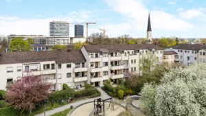 View over the rooftops of Munich-Berg am Laim with church tower and blooming trees in the courtyard – Rogers Immobilien