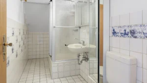 Small unrenovated bathroom with historical tiles and shower cabin in an apartment in Munich-Berg am Laim – Rogers Immobilien