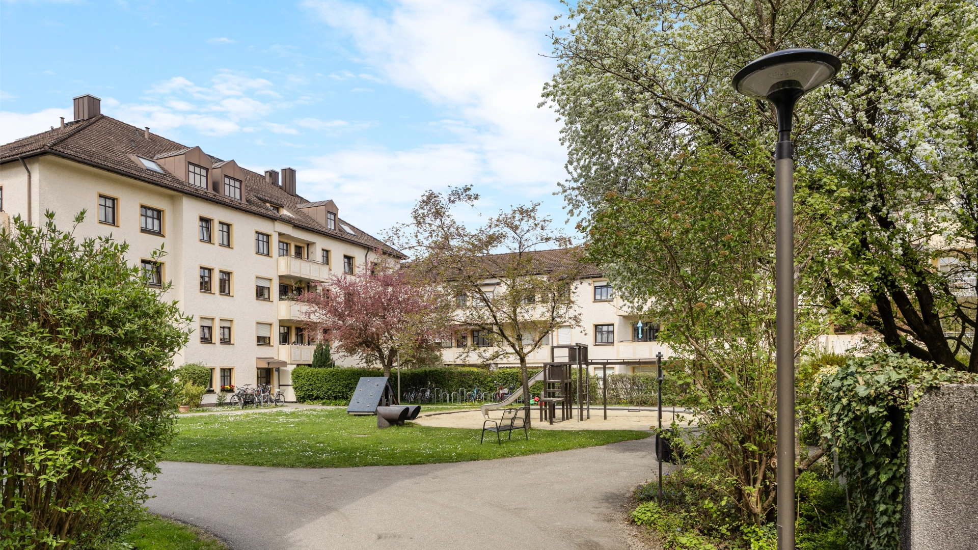Green space with a playground and bench in the inner courtyard of the residential complex in Munich-Berg am Laim – Rogers Immobilien