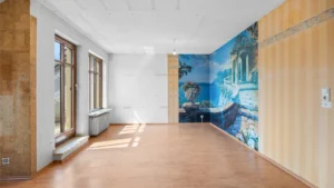Empty, unrenovated room with wooden flooring and decorative wallpaper in Munich-Berg am Laim – Rogers Immobilien