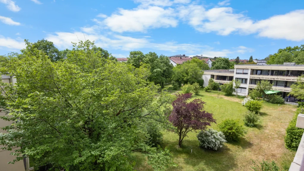 Blick vom Balkon über Bäume und Grünfläche auf das Nachbargebäude der Wohnanlage in Forstenried