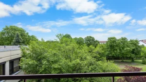 Blick vom Balkon über grüne Baumkronen bei blauem Himmel in der Wohnanlage München-Forstenried