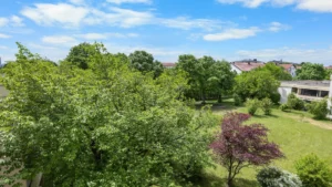 Blick vom Balkon über Baumkronen und Grünfläche zur Nachbarbebauung in München-Forstenried