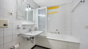 Kleines Badezimmer mit Fliesen, Badewanne und Waschbecken im unrenovierten Zustand in Forstenried