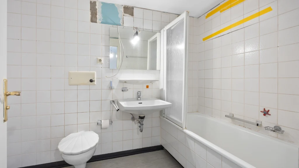 Bestehendes Badezimmer mit weißen Fliesen, Badewanne, WC und Waschbecken in München-Forstenried