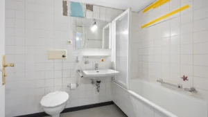 Bestehendes Badezimmer mit weißen Fliesen, Badewanne, WC und Waschbecken in München-Forstenried