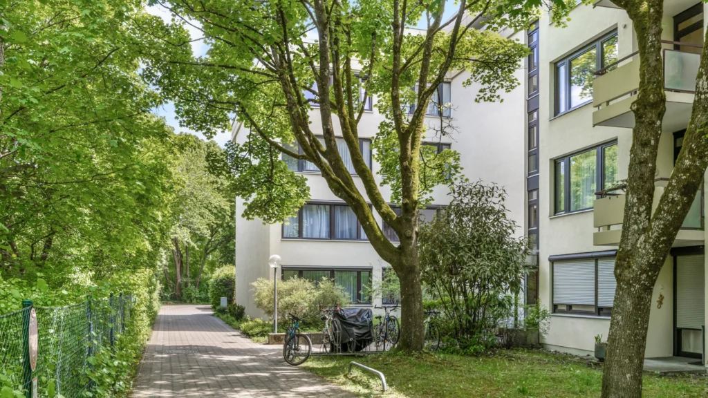 Gepflasterter Weg zwischen Bäumen führt zu den Wohngebäuden der Anlage in München-Forstenried