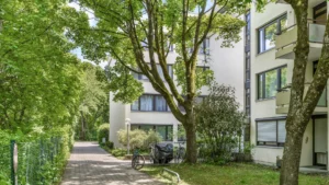 Gepflasterter Weg zwischen Bäumen führt zu den Wohngebäuden der Anlage in München-Forstenried