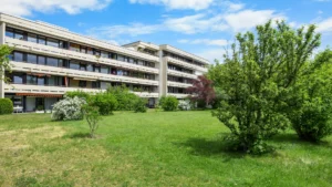 Weitere Hausansicht der Wohnanlage in München-Forstenried mit grüner Rasenfläche und blühenden Sträuchern