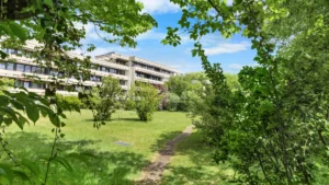 Hausansicht des mehrstöckigen Wohngebäudes mit Rasenfläche und Sträuchern in München-Forstenried