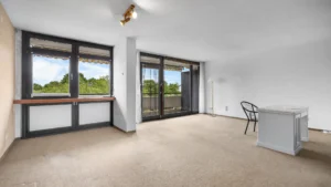 Leerer Wohnbereich mit großen Fenstern, Balkonzugang und Teppichboden in München-Forstenried