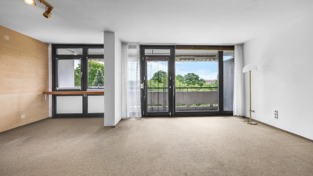 Leerer Wohnbereich mit raumhohen Fenstern, Balkonzugang und Grünblick in der Wohnung in München-Forstenried