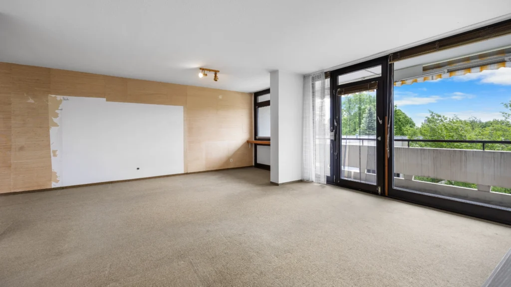 Leerer Wohnbereich mit Teppichboden, Balkonzugang und teilweise abgezogener Tapete in München-Forstenried